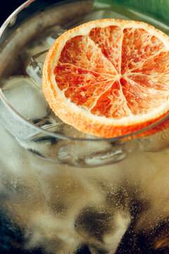 A slice of dried orange in a glass with a cocktail. Studio light.