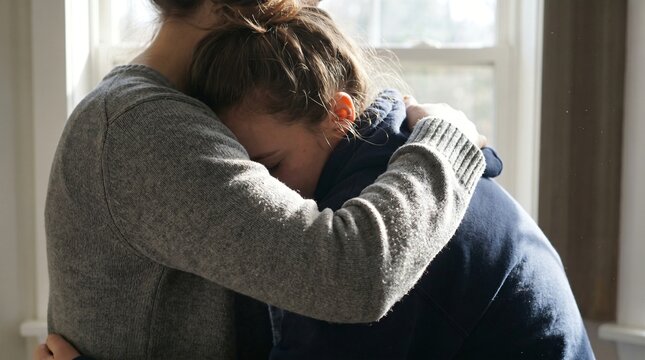 Close up of a supportive friend hugging and comforting a crying sad young woman.