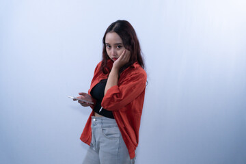 Naklejka premium Bored young woman holding smartphone and leaning face on hand on white background