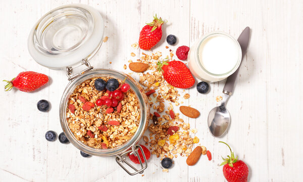 healthy breakfast granola in glass jar with fresh berries yogurt and almonds top view