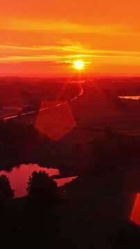 Beautiful golden sunset casting a pentagonal lens flare over a rural countryside landscape featuring small lakes, aerial view