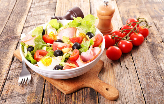 fresh mixed salad bowl with ham boiled egg, olives and tomatoes on rustic wooden table