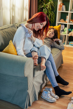 Mother tickling daughter's feet while sitting on sofa at home