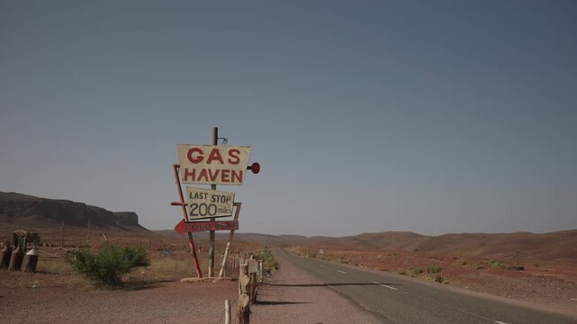 Vintage roadside gas station sign reads Last Stop 200 Miles beside empty desert road and rocky hills