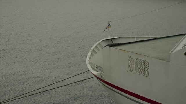White ferry bow with red stripe cuts through flat grey sea under overcast sky with mooring ropes visible