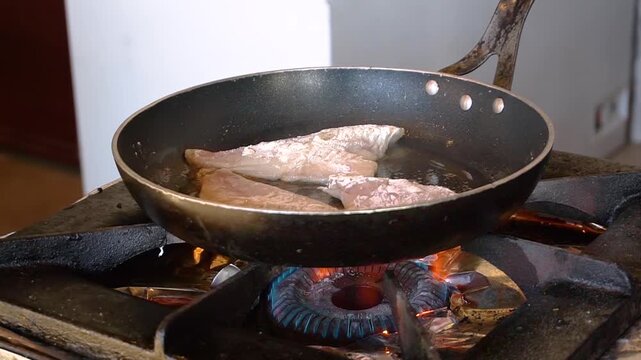 Chef frying fish in a pan in restaurant kitchen