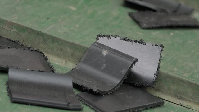 Individual flat black plastic shredded sheets with jagged edges scattered across worn green conveyor belt