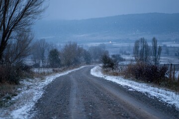 Obraz premium Gravel road in a snowy landscape with drifting flurries