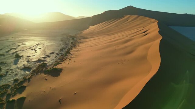 Drone flies over the dead valley of orange desert with orange sand at dawn with a beautiful sun