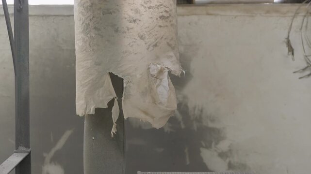 Torn and shredded dirty plastic film falls through industrial recycling machine chute in close up