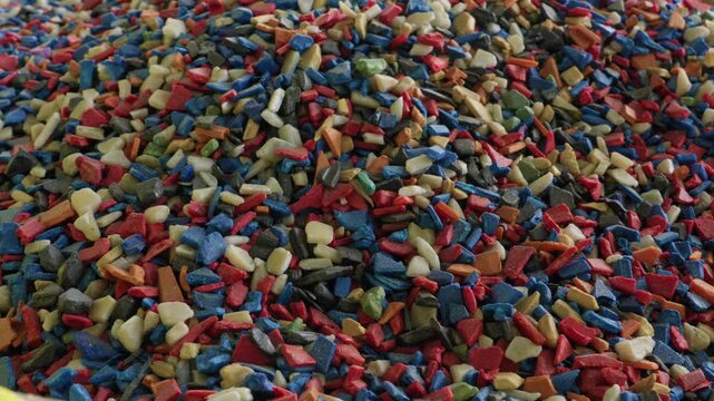 Dense pile of colorful mixed recycled plastic granules in red blue beige green filling entire frame