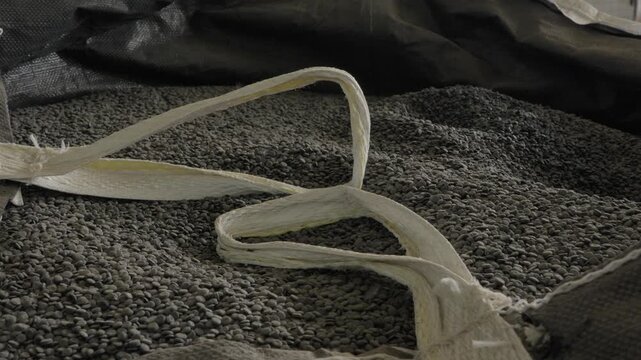 White torn bulk bag straps lie across dense dark grey recycled plastic granule pile in recycling factory
