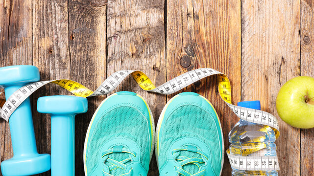 running shoes with dumbbells measuring tape and apple on rustic wooden table fitness concept