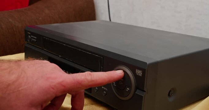 Finger pressing the play button on a VHS VCR front panel. Analog video playback and retro media technology