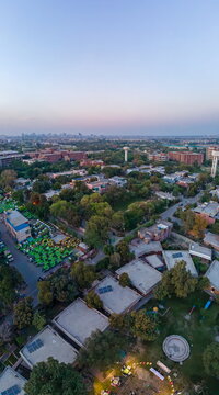Aerial view of the urban landscape featuring residential rooftops, lush green trees, and the distant Arfa Kareem Tower skyline during twilight in Lahore, Punjab, Pakistan.