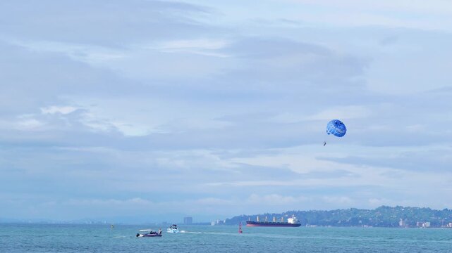 Blue parasailing parachute flying over a calm sea with distant ships