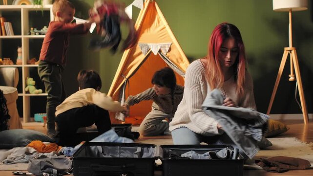 Stressed mother packing suitcase while children playing at home