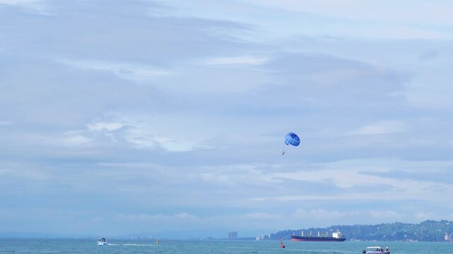 Blue parasailing parachute flying over a calm sea with distant ships
