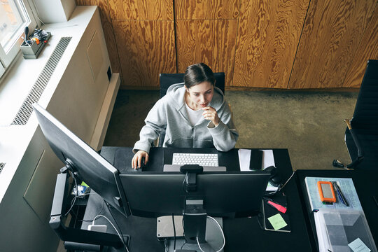 High angle view of female business professional working on dual computer while sitting at desk in tech startup office