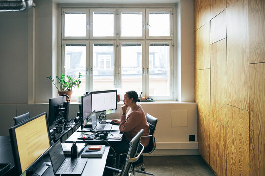 Focused female corporate expert using multiple technologies while sitting at desk in office