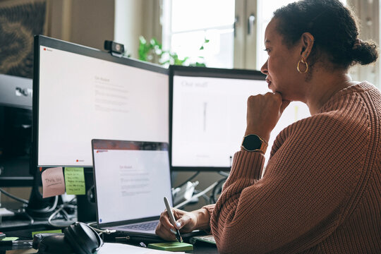 Concentrated female expert reading details on computer screen while writing notes in startup office