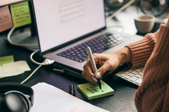 Hand of businesswoman writing on adhesive note while working in tech office