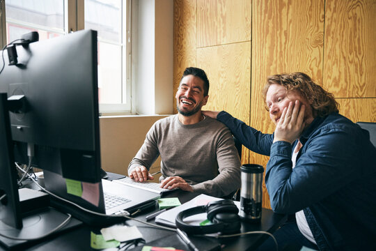 Happy mature businessman sitting with coworker at office desk
