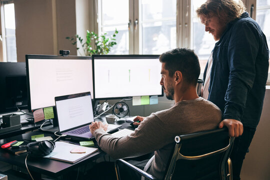 Male tech professionals comparing design models on multiple devices while working in startup office
