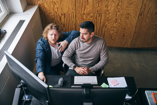 High angle view of male tech professional sharing ideas with coworker through computer while sitting in office