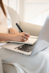 Fototapeta premium Close up of woman's hand holding pen writing in notebook over laptop on sofa in cafe or living room