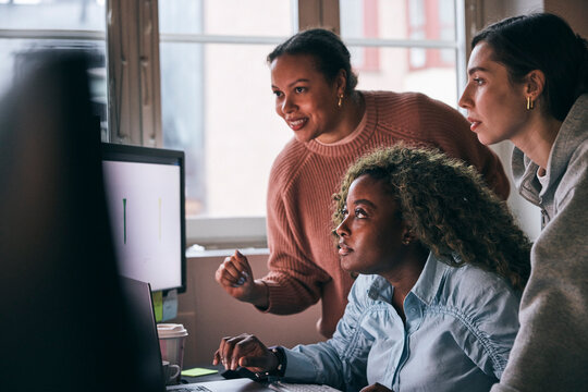 Multiracial female tech professionals analyzing details on computer while working in startup office