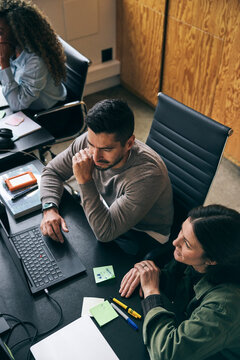 High angle view of male and female business expert discussing ideas with each other while working on laptop in startup o