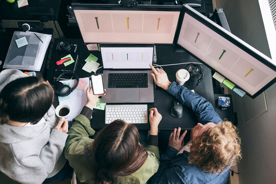 High angle view of male and female tech experts checking design previews on devices while working in startup company