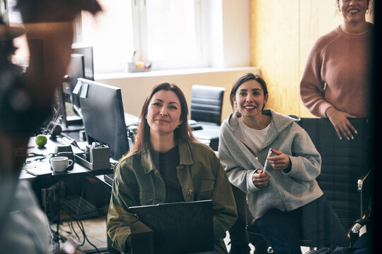 Smiling female business expert sitting in meeting with coworkers at tech startup office
