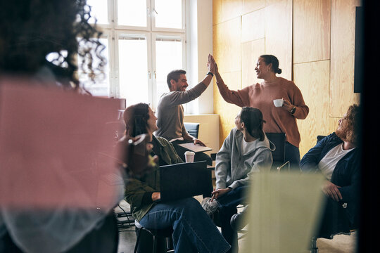 Female tech expert giving high-five to male colleague during office meeting