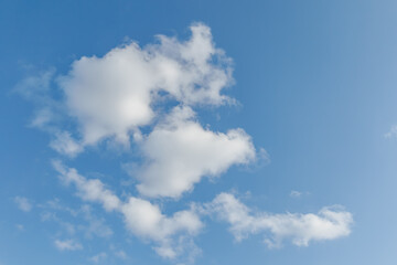 Fototapeta premium Scattered white cumulus clouds drifting across a clear bright blue sky on a sunny day