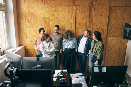 Team of business experts talking with each other while standing near brown wall in startup office