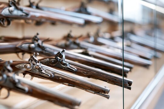 Collection of antique flintlock pistols displayed in a museum case, showcasing historical weaponry.