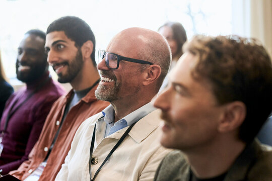 Smiling senior businessman wearing eyeglasses attending seminar with other executives in convention center