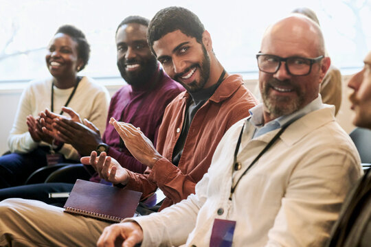 Smiling businessman clapping while attending corporate seminar with colleagues in convention hall