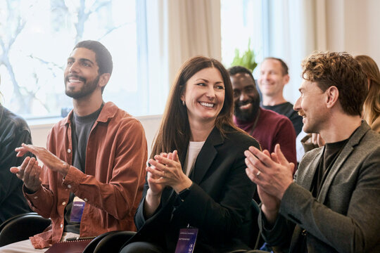 Smiling businesswoman clapping while attending corporate seminar with colleagues in convention hall