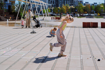 Obraz premium Young girls playing hopscotch on a sunny day in a contemporary city park.