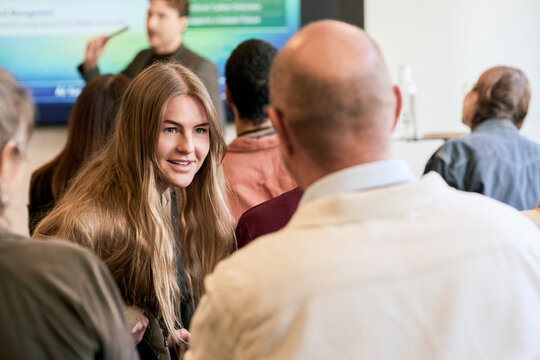 Long haired female entrepreneur talking with senior associate while looking over shoulder during seminar in convention c