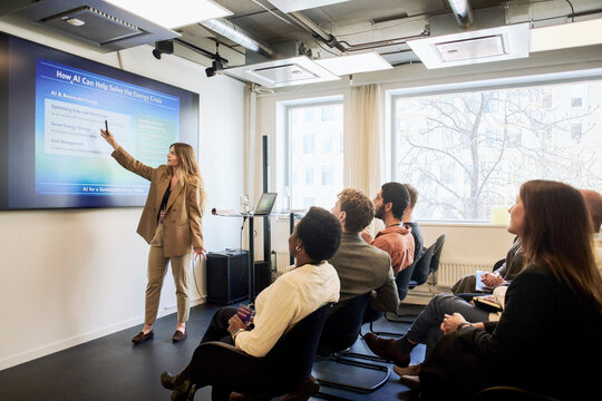 Full length of female presenter explaining slide show points to business executive through projection screen in conferen