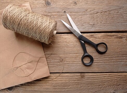 Top view of some recycled and biodegradable packaging materials like linen string and recycled paper bag on the wooden table with scissors.