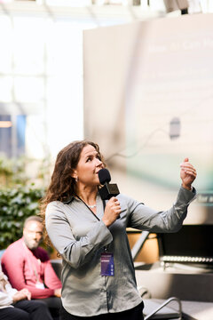 Mature female speaker discussing presentation points with audience while speaking into microphone during summit in congr