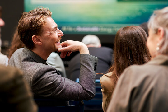 Smiling male business expert sitting in seminar with hand on chin at convention center