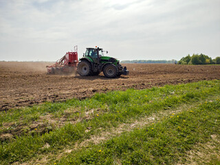 Fototapeta premium Tractor pulling a seeder machine across a field. Farmer planting seed in soil during spring season. Modern agricultural equipment