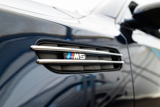 Lucerne, Switzerland, May 30, 2026. Tricolor BMW M5 model badge on the chrome side fender vent grille of a blue sedan.