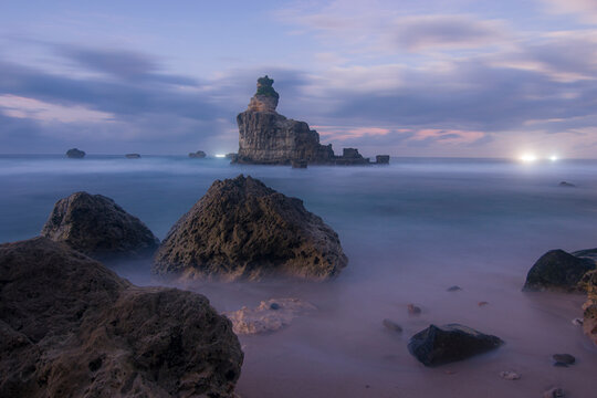 Stunning coastal landscape at Buyutan Beach, Pacitan, showcasing a towering sea stack, turquoise waters, rocky shoreline, and cloudy evening atmosphere.